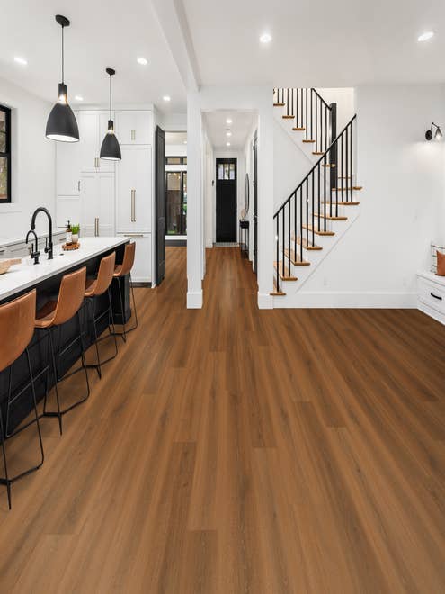 Modern-style staircase, entryway, and black-and-white kitchen island with leather chairs pulled up and medium toned lamiante floors
