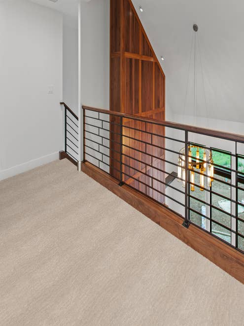 Alistair Stone colored carpet in hallway with white walls and a wooden accent wall with black stair railing.