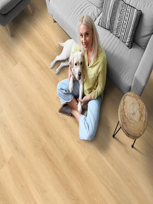 Woman with dog on her lap sits on a light-color wood-look LVP and leans against a modern gray sofa