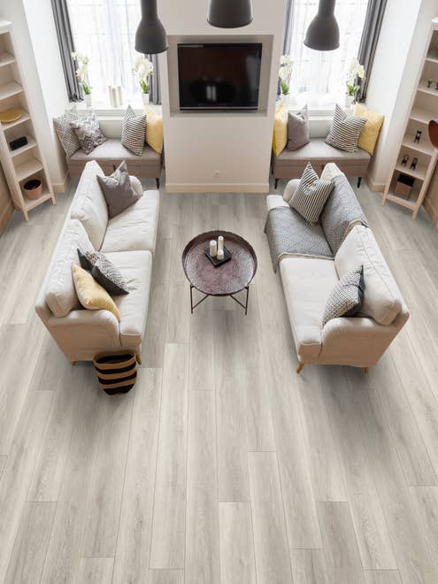 Living room with two couches facing each other, a television on the wall, window seats, and vertical bookcases, over light gray wood-look vinyl plank flooring