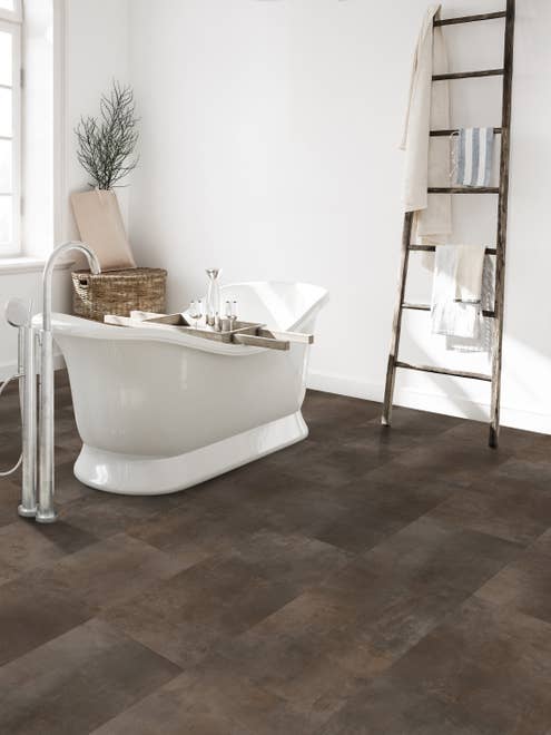 Modern white bathroom with a white free-standing bathtub, a rustic ladder shelf with towels, and a brown tile-look LVT floor