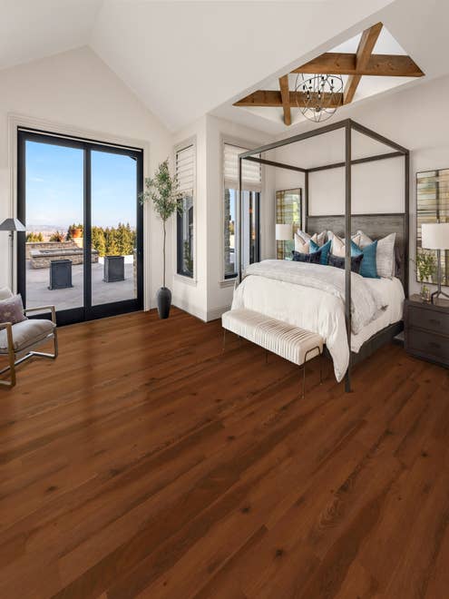 Bedroom with four-poster bed, dark cherry luxury vinyl plank floors, and a set of sliding glass doors overlooking an outdoor patio