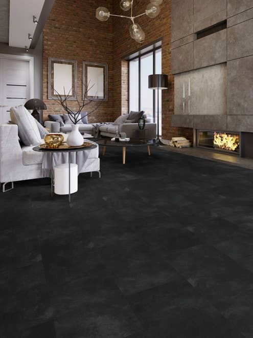 Industrial-inspired living room with exposed brick walls, large modern concrete fireplace, couches, and black and charcoal stone-look tiles