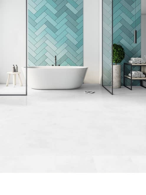 Free-standing white bathtub set against a wall with various shades of light blue herringbone tile and bright white tile LVT flooring