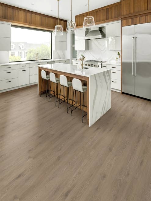 Modern organic wood and white kitchen with marble island, chairs, large window, refrigerator, over gray-brown wide-plank floor