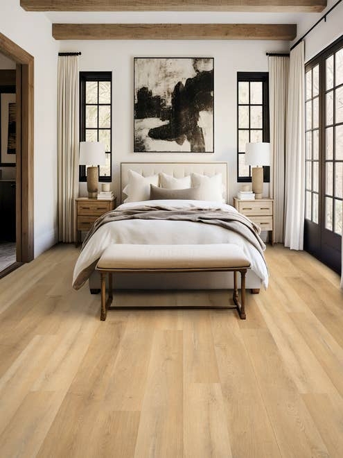 Inviting bedroom with white walls, pale tan woodgrain floors, wooden beams, black-framed windows, modern art, and an organic-inspired bedroom set
