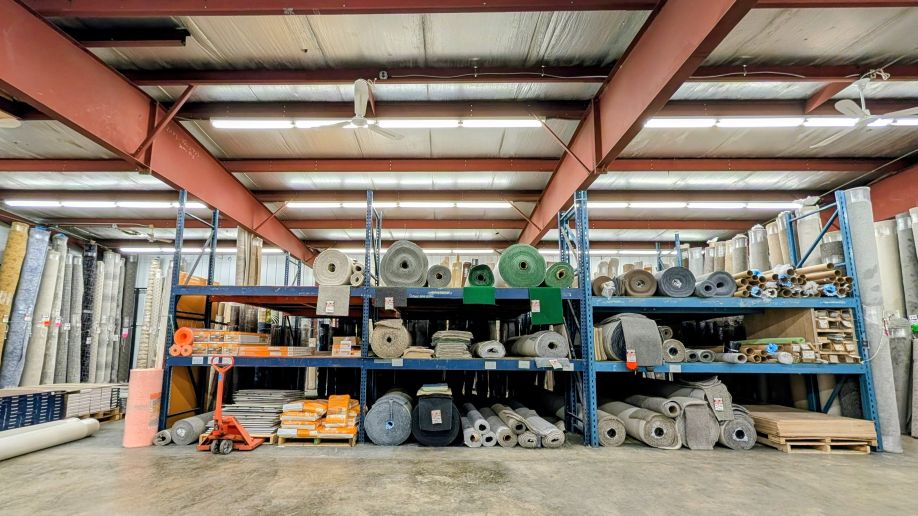 Carpet rack at Mullen's Factory Direct Flooring showing rolls of carpets on shelves in various colors