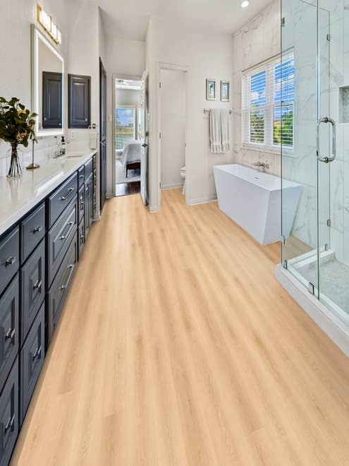 Modern bathroom with blue vanity, glass shower, white tub, and warm-toned tan woodgrain LVP flooring