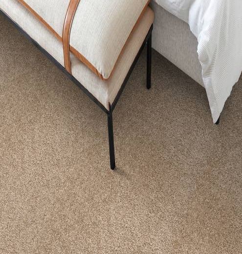 Overhead photograph of ottoman at end of bed, on tan solid plush carpet
