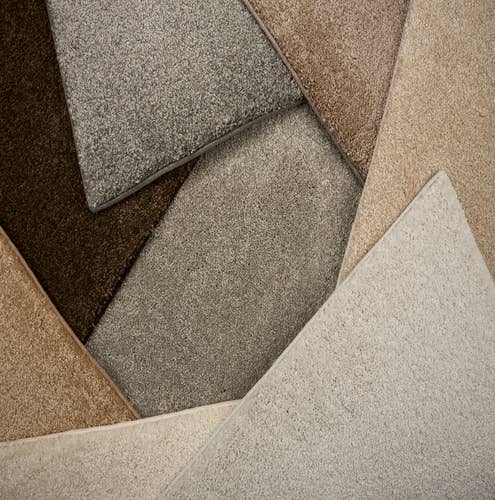 Overhead photograph of a pile of bound textured carpet samples in grays, tans, and browns