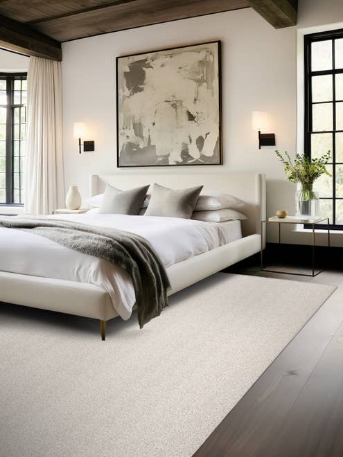 Modern bedroom scene with bed, moder artwork, dark wood floors, and a light gray textured area rug