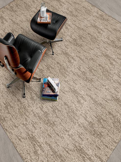 Modern leather chair and ottoman and stack of books on a abstract patterned textured taupe carpet.