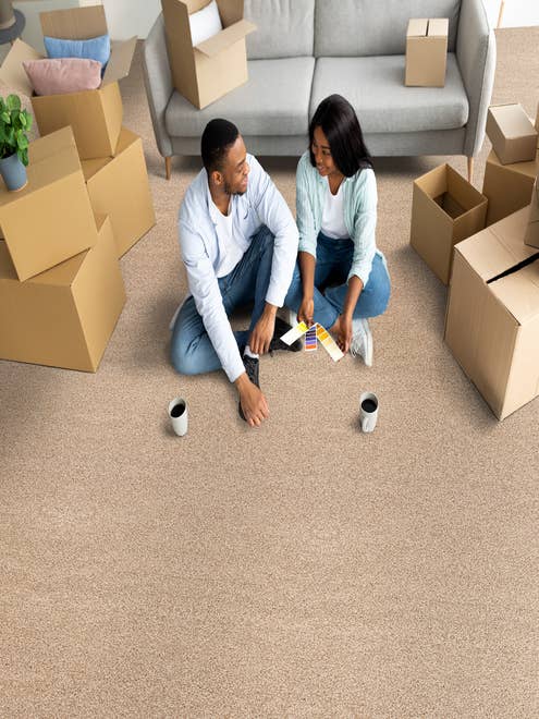 Young couple sitting on solid texture tan carpet with coffee mugs and moving boxes