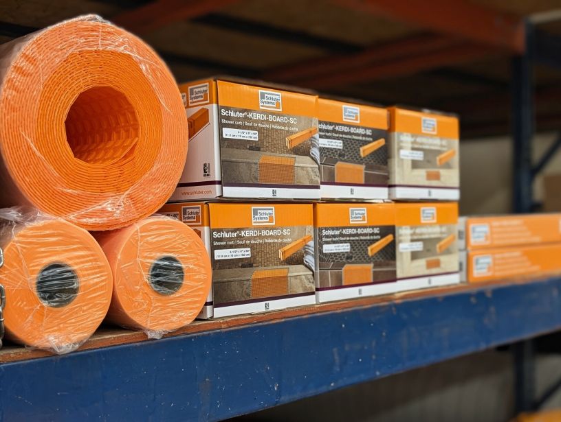 Stacked Schluter items on a shelf in orange, grey and white packaging