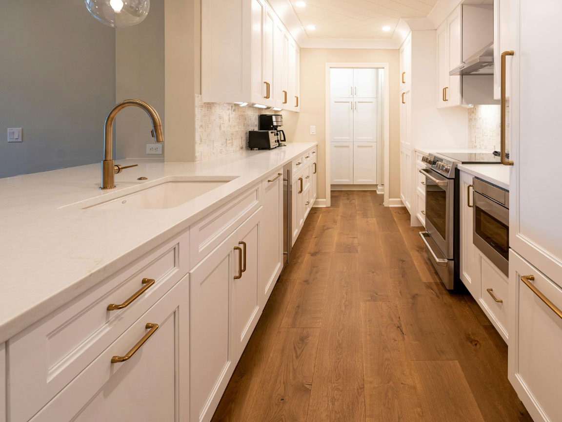 Kitchen cabinetry, white cabinets with gold hardware, dark colored wooden floor, silver appliances