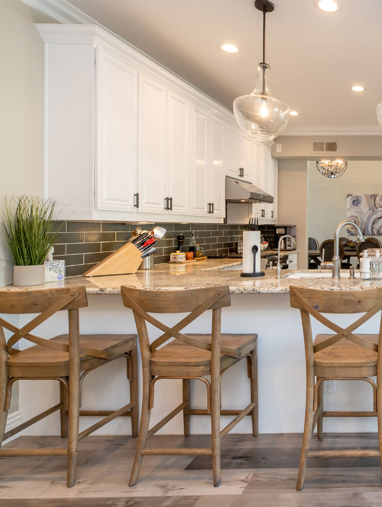 Kitchen cabinetry, white cabinets with dark hardware, wooden bar stools by kitchen counter