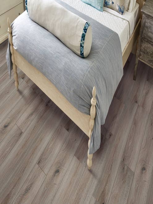 Inviting bed, with pale blue comforter, large pillows, and rustic wooden frame on weathered beige LVP