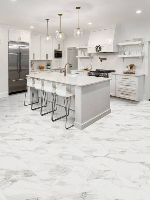 White modern kitchen designed with farmhouse influence, featuring white shaker cabinets, a white island, and Cararra Baino LVT floors
