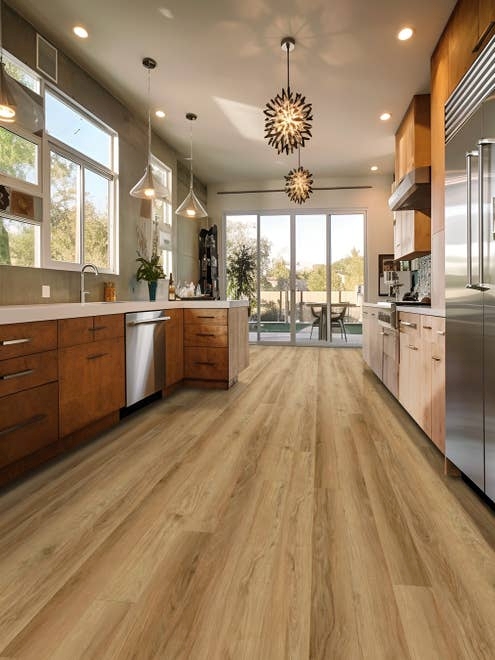 Mid-century modern inspired kitchen with clean, subtle brown woodgrain flooring, textured chandeliers, pendant lights, and sliding glass doors leading to patio