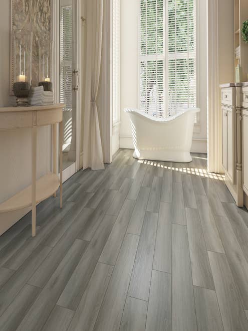 Airy, spa-like bathroom with free-standing tub before large window, with medium and light gray plank flooring