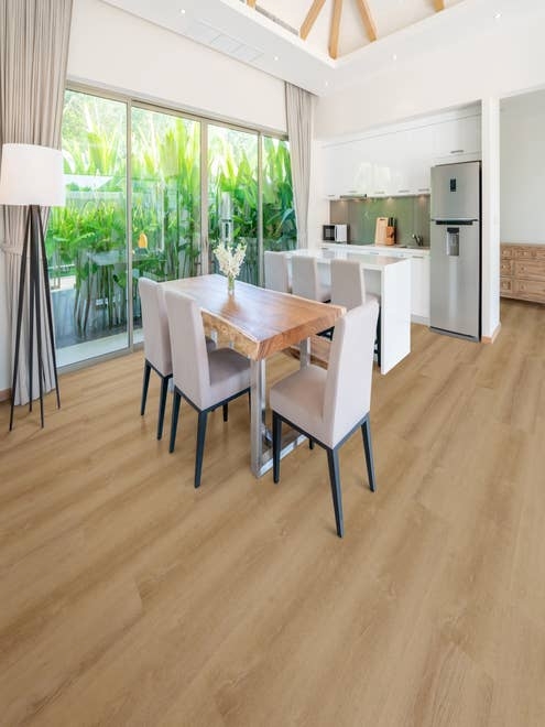 Open-concept white kitchen and contemporary dining table and chairs, placed before large glass doors showing vibrant tropical foliage