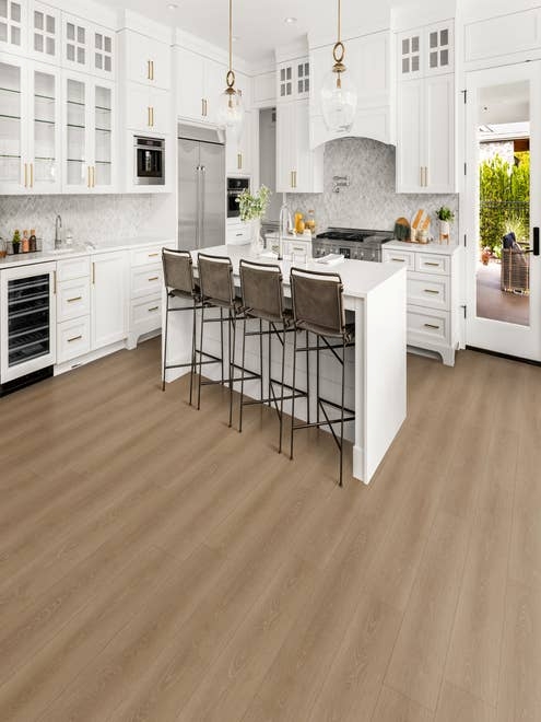 Luxury modern white kitchen with gold accents, with island seating area, over warm brown woodgrain laminate, with view of side porch