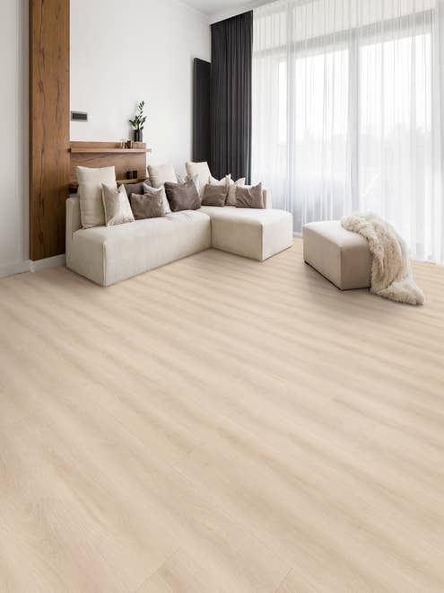 Cozy, bright, airy room with couch laden with pillows and a fur blanket, on cream woodgrain floor