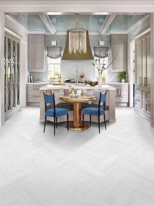 Kitchen with large silver chandelier, island seating, gray cabinetry, and white herringbone floor