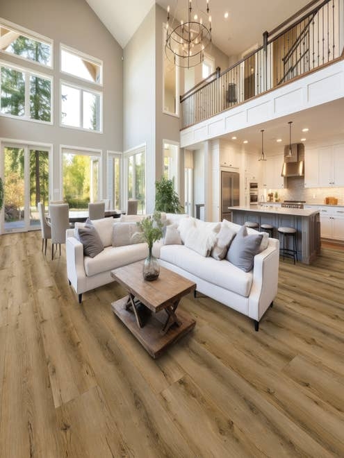 Open-concept living room, kitchen, and dining area with beige weathered floors and large windows showing wilderness beyond,