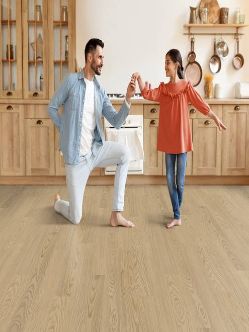 Man kneels to hold young girl's hand as she dances in a country kitchen with light wood cabinets and light Oakridge Antique Linen floor