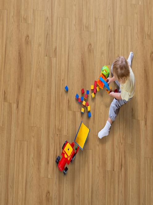 Boy sits on warm, gold laminate floor and plays with toys