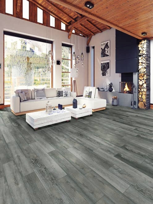 Living room with white sectional, tall wood ceilings, firewood stacked beside modern fireplace, glass pendant lighting, and blue-gray woodgrain Rockwood Bluestone flooring, with large windows showing outdoors