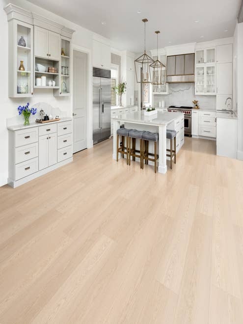 Modern white kitchen with oversized metal chandeliers, central island with seating, and pale beige woodgrain LVP floors