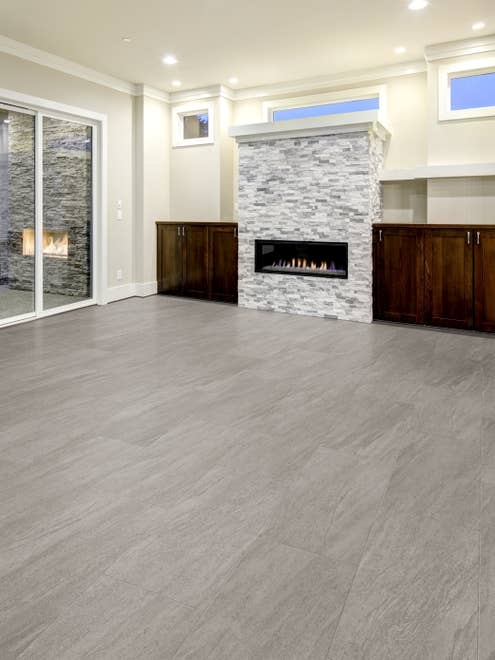Open gathering area with large gray stone fireplace and dark wooden built-in cabinets, beside sliding glass door, in room with light gray stone-look LVT floor