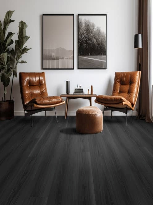Two leather chairs, a small table, an ottoman, and a potted plant on a black woodgrain floor, in room with two black and white photos on white wall