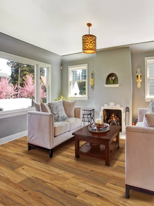 Cozy, calm living room with large windows, golden brown floors, two couches facing a wooden coffee table before a fireplace, with sconces and a patterned chandelier