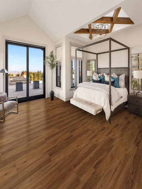 Bright, airy bedroom with large bed, nightstand, and armchair, over LVP floor with varying brown tones, with large glass doors leading to patio