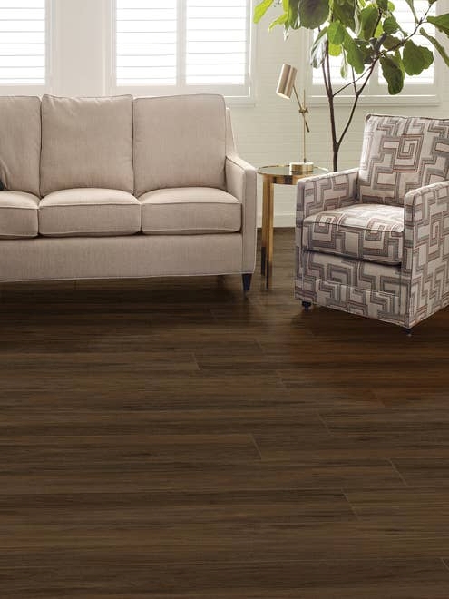 Couch, armchair, and houseplant in bright living room with dark, rich woodgrain LVP floor