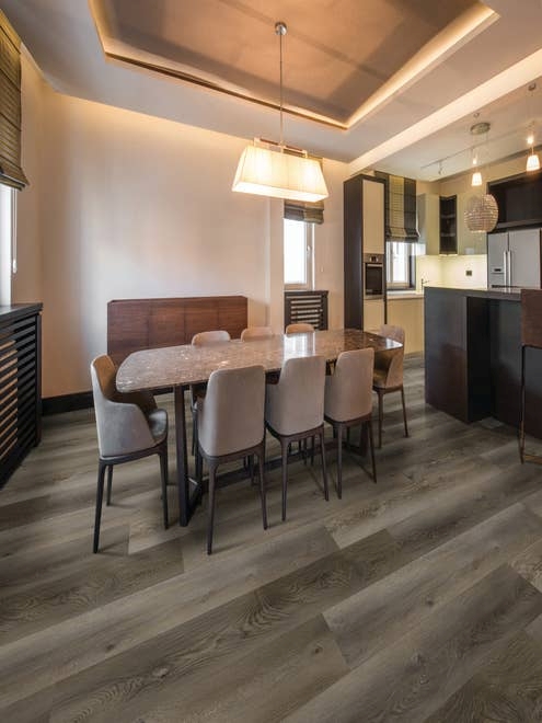 Dining table and chairs near black kitchen cabinets, with recessed lighting, rectangular chandelier, with medium gray woodgrain LVP floors, in cozy, moody space