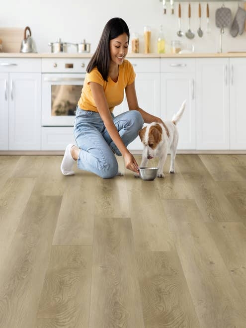Woman kneels before modern white kitchen cabinets with wooden countertops and feeds small dog