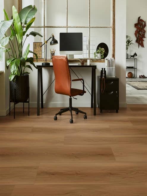 Home office with leather chair, computer desk, storage cabinet, and large potted plant in room with natural light a rich, warm wood-look LVP flooring