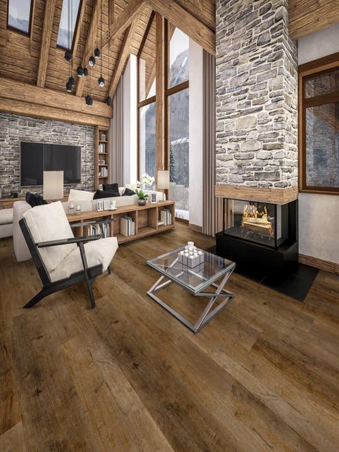 A-frame cabin with large fieldstone fireplace and accent wall, with armchair, bookshelf, couch, and television, with wooden ceilings, medium brown wood-look LVP floor, and floor-to-ceiling windows