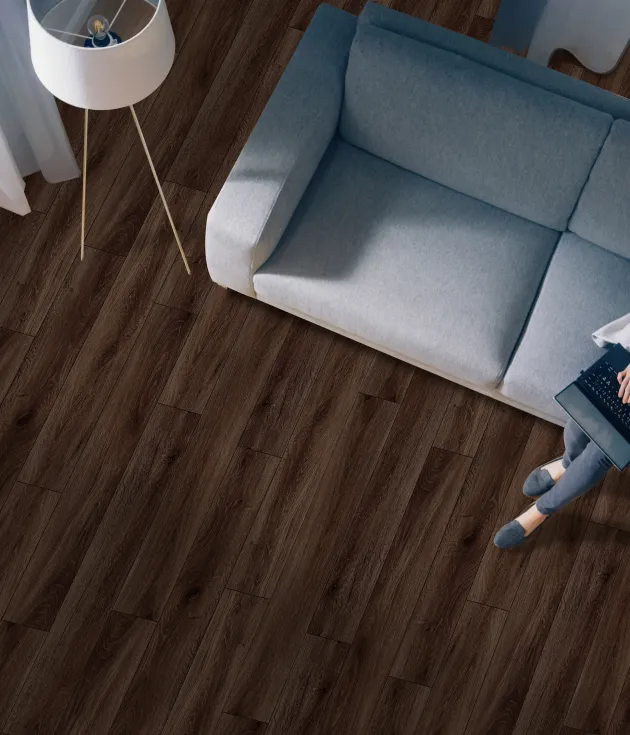 Woman sits on couch and works on laptop beside floor lamp, in calming room with blue walls and rich walnut-color LVP floor