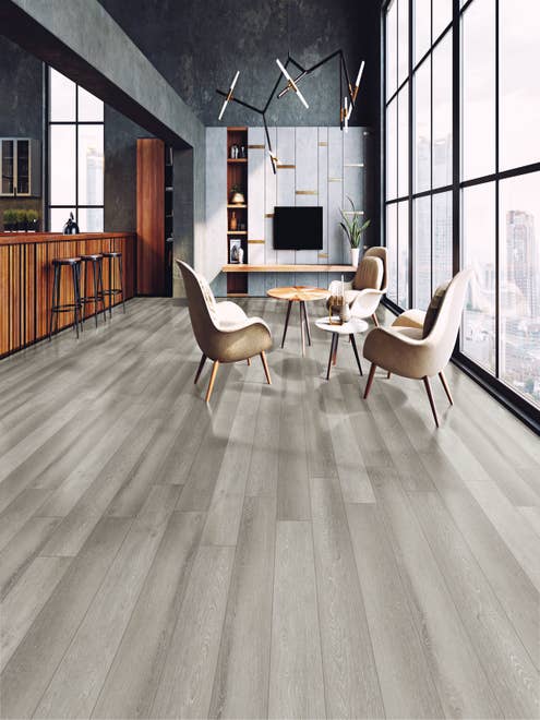 Modern open concept apartment with windows overlooking cityscape, with multiple armchairs and side tables beside kitchen island barstools, built-in shelving in background, black architectural beam, and light gray woodgrain LVP flooring