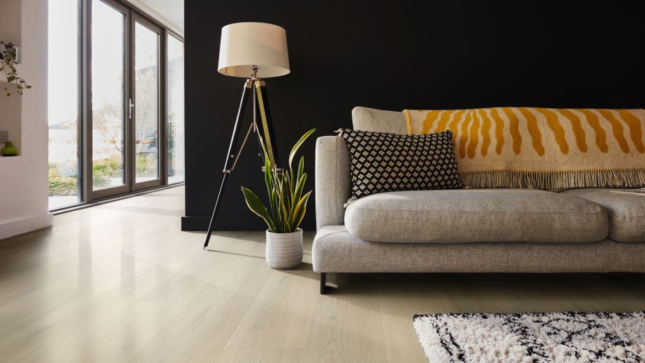 Living room with black wall, light beige/taupe woodgrain floor, gray mid-century sofa, potted plant, and floor lamp