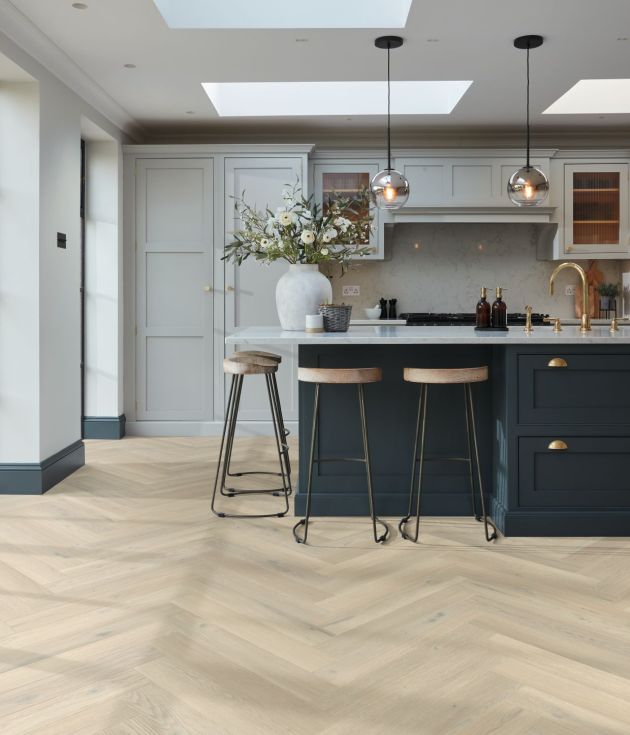 Kitchen with large bright windows, sky lights, pendant lights, built-in cabinets, and blue island with barstools over taupe/beige herringbone woodgrain floor
