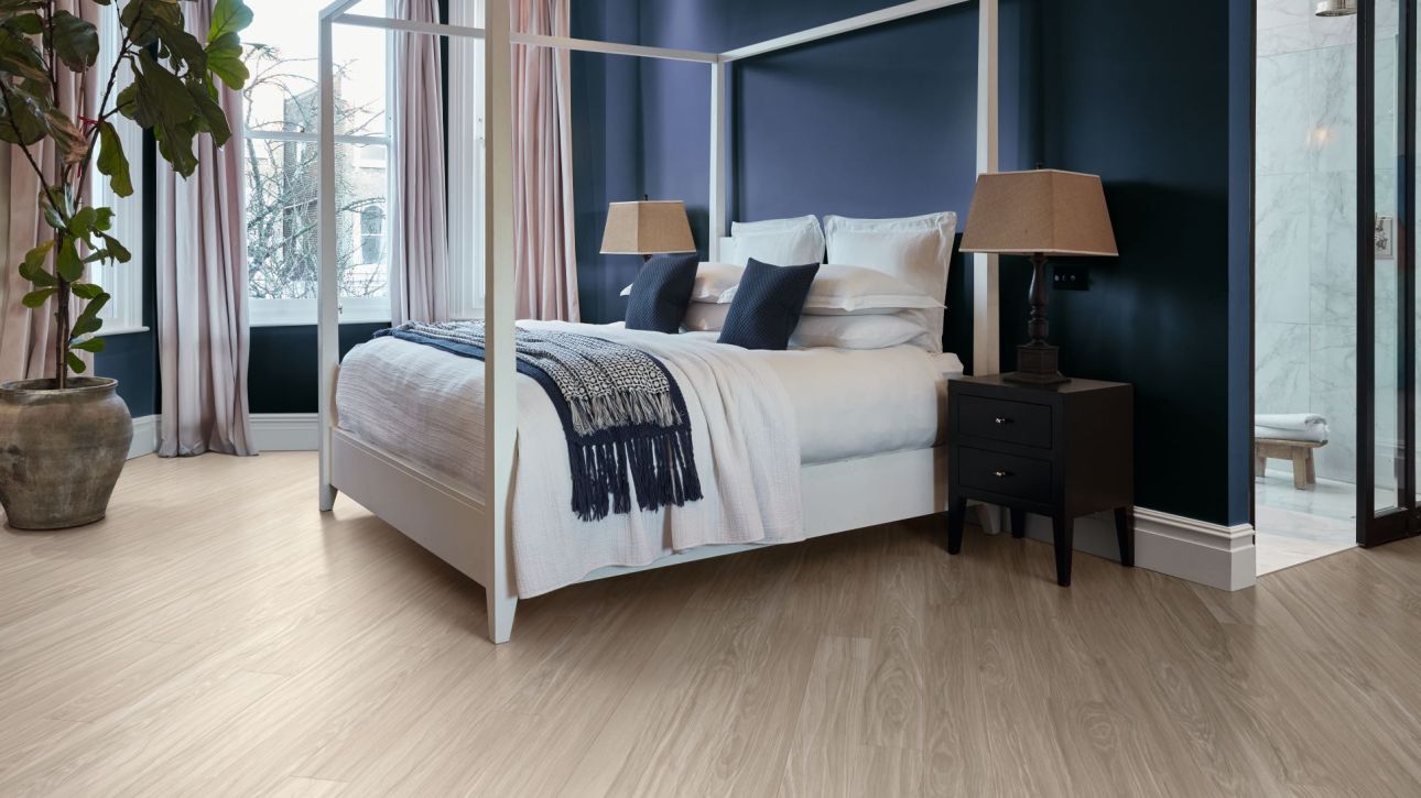 Calm bedroom with dark blue walls, gray woodgrain floors, cozy bed, night stands, large plant, and window
