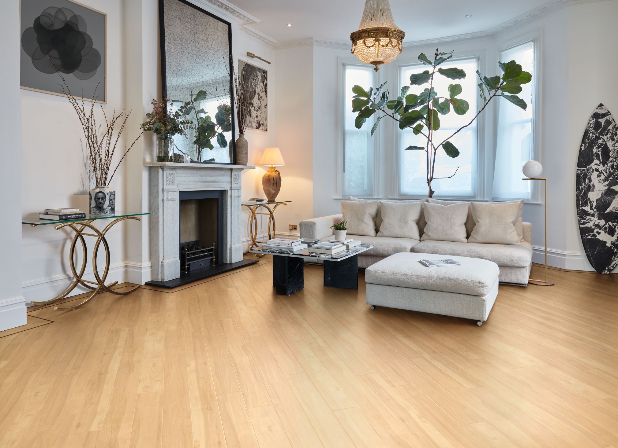 Living space with antique chandelier, off-white walls, pale golden woodgrain floor, white sofa, large houseplant, and fireplace topped with mirror