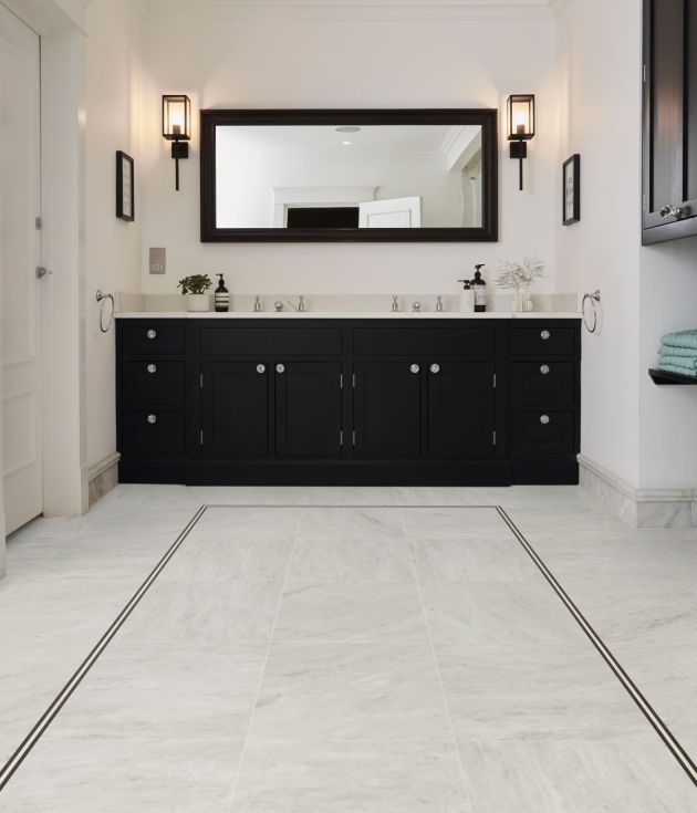 Bathroom with black dual sink vanity, black sconces, and large black-rimmed mirror, with white marble-look LV floors and an inlaid black design border