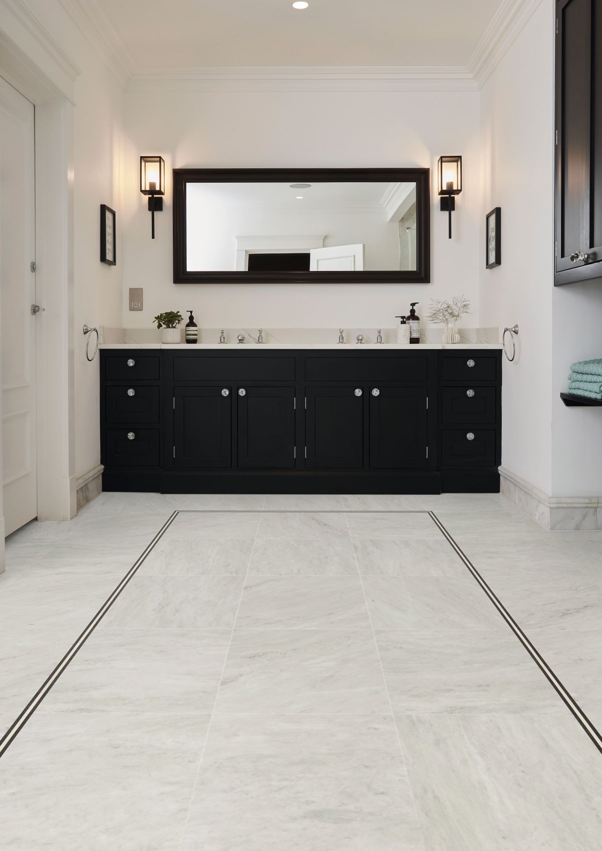 Bathroom with black dual sink vanity, black sconces, and large black-rimmed mirror, with white marble-look LV floors and an inlaid black design border